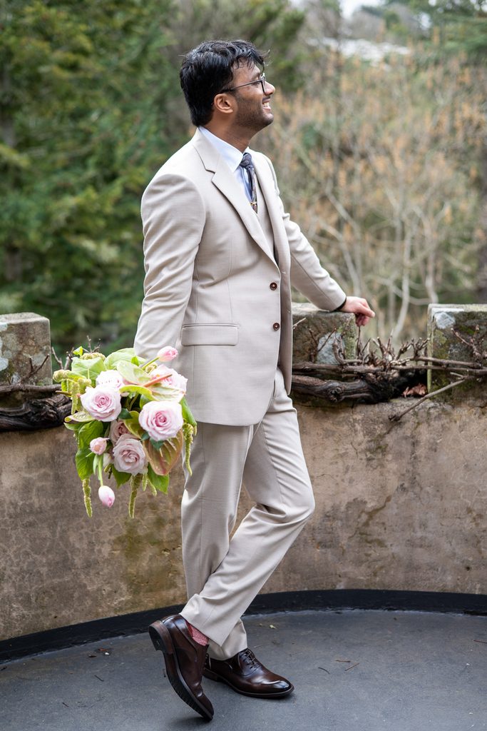 Groom posing on a balcony holding a bouquet of flowers